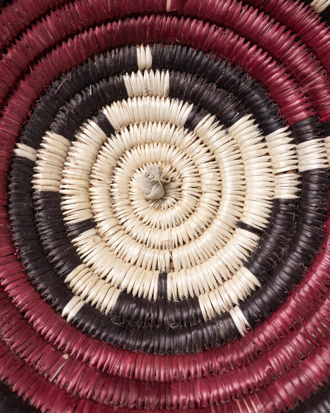 A vintage Navajo coiled basket with a starburst pattern in natural, red, and black tones, center close up of basket.