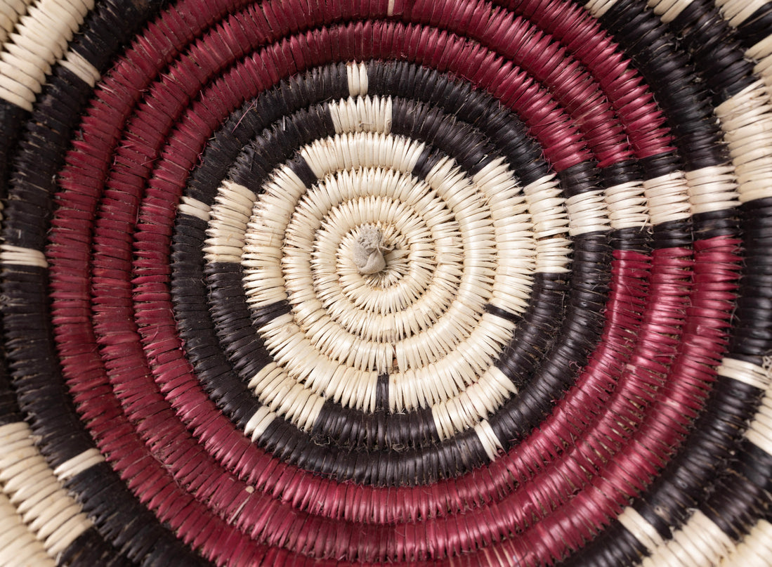 A vintage Navajo coiled basket with a starburst pattern in natural, red, and black tones, center close up of basket.