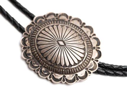 Close-up of a Navajo silver bolo tie with intricate stamp design on a white background