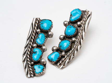 Pair of Native American old-fashioned silver stamped earrings with turquoise stones on a white background