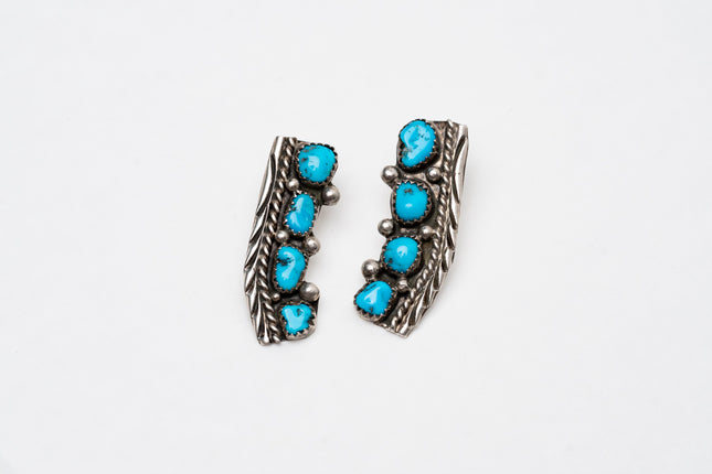 Pair of Native American silver stamped earrings with turquoise stones on a white background