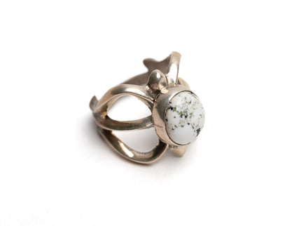 Top view of silver cast cut-out ring showcases a single, centrally set round white buffalo stone on a white background. Ring appears gold because of the natural patina