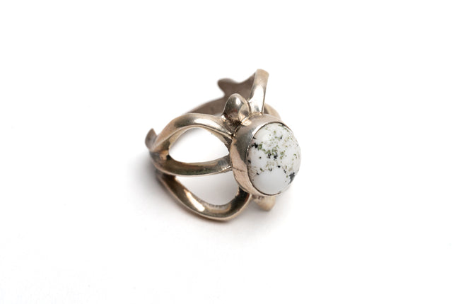 Top view of silver cast cut-out ring showcases a single, centrally set round white buffalo stone on a white background. Ring appears gold because of the natural patina