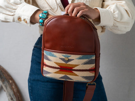 Person wearing a turquoise bracelet holding a Pendleton brown backpack with a colorful woven pattern