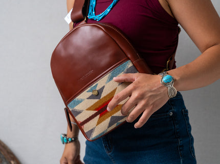 Person holding a Pendleton brown leather bag with a colorful pattern in front of their body, wearing a turquoise bracelet