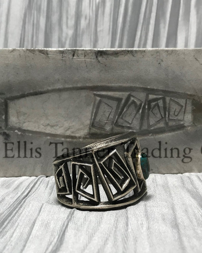 A silver Cuff with a rough silver square maze cutout. In the center is a round Royston Turquoise stone. side view 