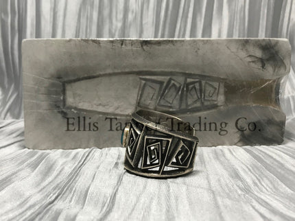 A silver Cuff with a rough silver square maze cutout. In the center is a round Royston Turquoise stone. side view 