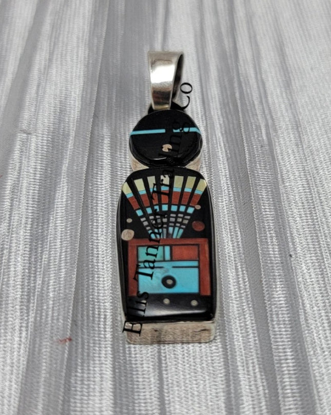 A silver pendant with a Navajo deity inlay pattern, featuring an array of colors including black, white, red, and blue.