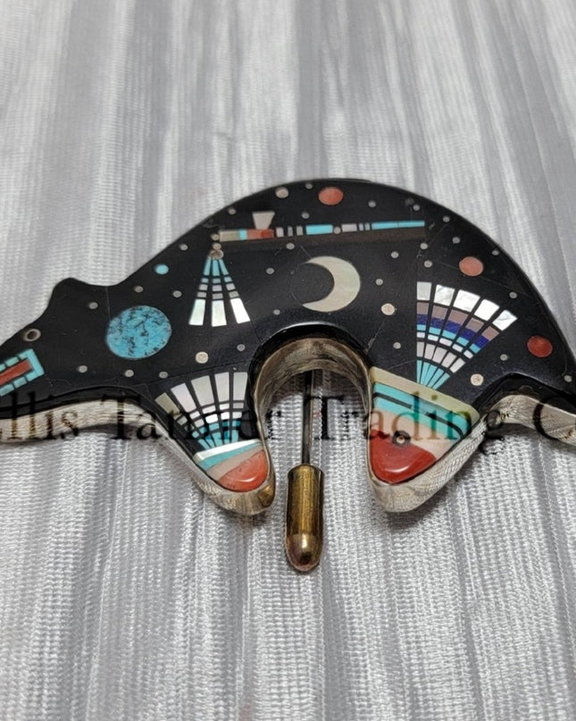 A silver pin with an inlayed bear design featuring various stones such as onyx, mother of pearl, coral, pink shell, and abalone lapis.