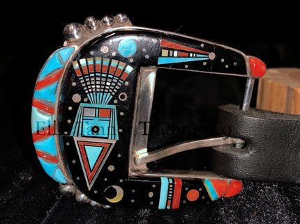 A handcrafted Ranger belt buckle set featuring intricate inlay work. The design incorporates vibrant geometric patterns with black, turquoise, coral, and white inlays, inspired by Southwestern artistry. The bold and colorful patterns are framed by polished silver, enhancing the intricate details. The set is displayed on a black leather belt, resting on a textured dark background.
