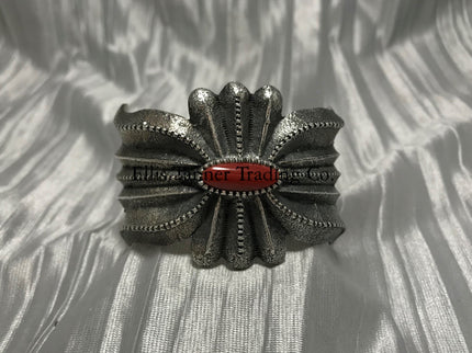 A silver-colored cuff bracelet with a central coral stone, on a textured silver background.