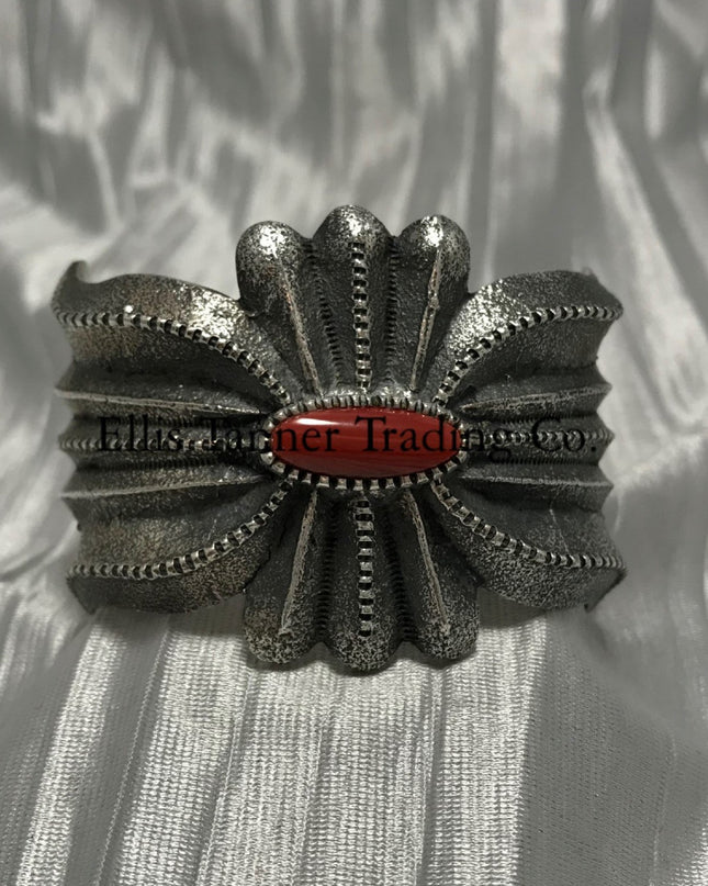 A silver-colored cuff bracelet with a central coral stone, on a textured silver background.