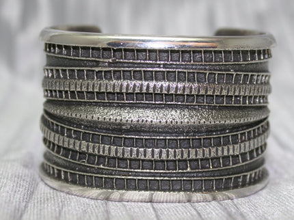 Large Sand Cast Cuff. Crafted from sterling silver using the sand cast technique, this cuff features unique texture and shine, on a shiny silver cloth.