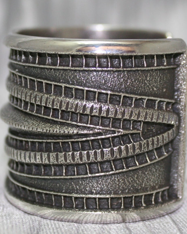 Large Sand Cast Cuff. Crafted from sterling silver using the sand cast technique, this cuff features unique texture and shine, on a shiny silver cloth.