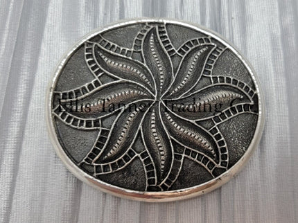 Silver sandcast, spiral flower, buckle placed on top of a silver cloth.