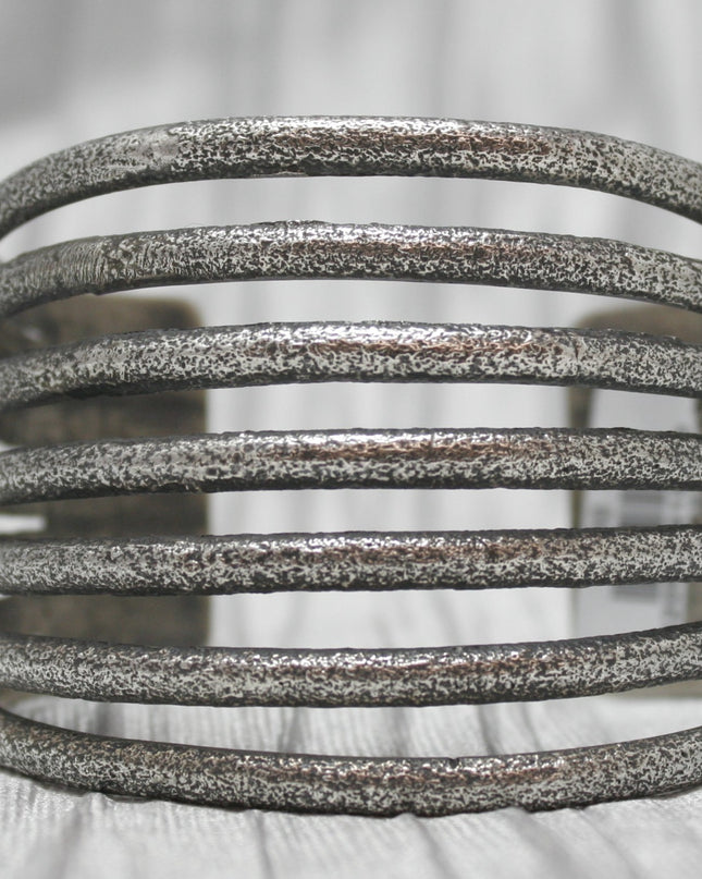 A multi-band silver cuff bracelet with a textured, rustic finish, featuring evenly spaced horizontal bands stacked in an open design. The bracelet is showcased against a soft, neutral background, emphasizing its unique craftsmanship and versatile style. 