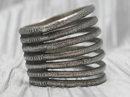 A multi-band silver cuff bracelet with a textured, rustic finish, featuring evenly spaced horizontal bands stacked in an open design. The bracelet is showcased against a soft, neutral background, emphasizing its unique craftsmanship and versatile style.