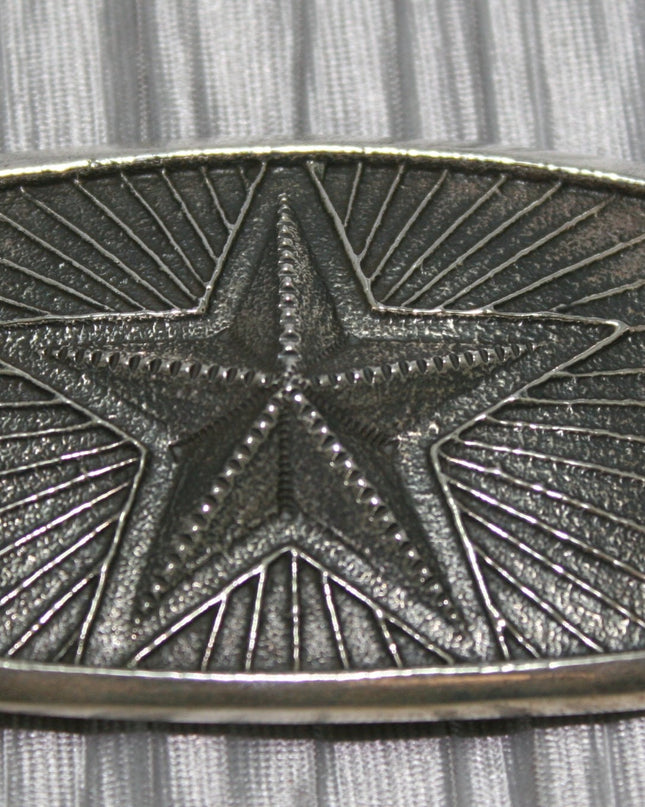 Silver belt buckle featuring a raised five-point star in the center, surrounded by radiating lines in a textured background.