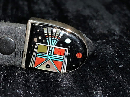 A handcrafted Ranger belt buckle set featuring intricate inlay work. the design incorporates vibrant geometric patterns with black, turquoise, coral, and white inlays, inspired by Southwestern artistry. The bold and colorful patterns are framed by polished silver, enhancing the intricate details. The set is displayed on a black leather belt, resting on a textured dark background.