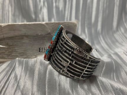 Displayed is the side of a silver tufa cobbletone bracelet, on a silver shiny sheet,