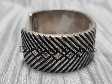 heavy, etched diamond designs front view of bracelet, displayed on top of a silver shiny cloth, side 
