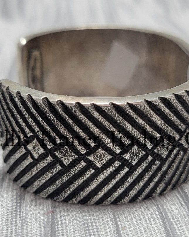 heavy, etched diamond designs front view of bracelet, displayed on top of a silver shiny cloth, side 
