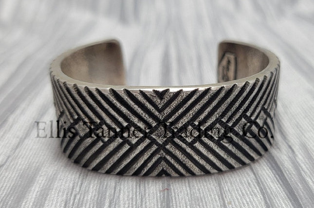 heavy, etched diamond designs front view of bracelet, displayed on top of a silver shiny cloth.