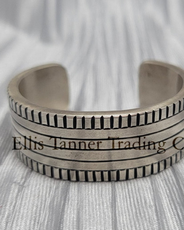 Front View of a heavy silver stamped bracelet, placed on a silver cloth 