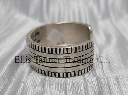 Side of a heavy silver stamped bracelet, placed on a silver cloth 