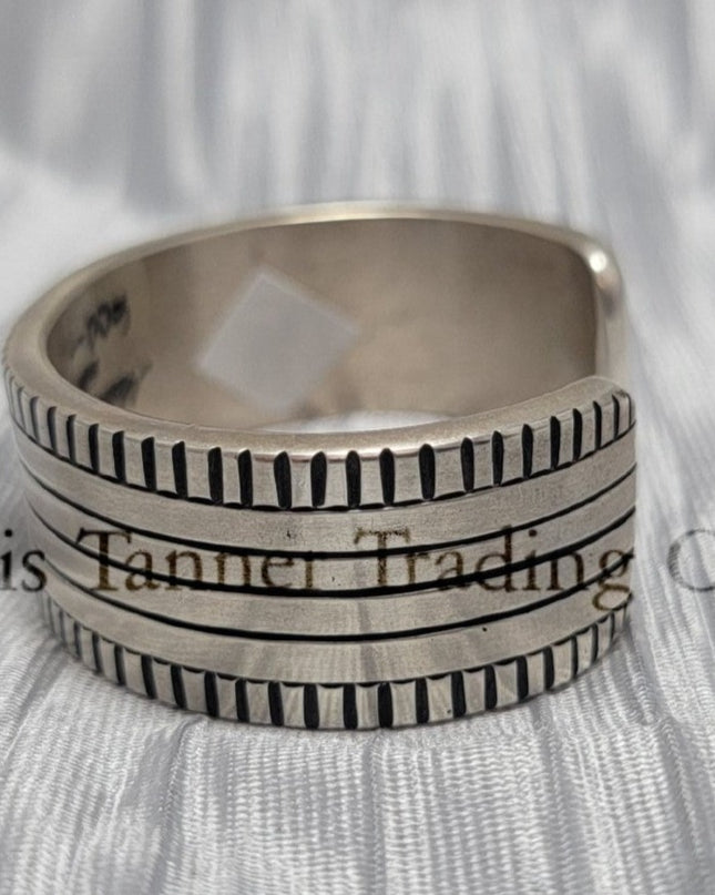Side of a heavy silver stamped bracelet, placed on a silver cloth 