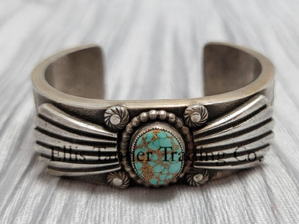 Heavy silver bracelet, with a center Carico Lake Turquoise stone, with an overlay design, on top of a shiny silver sheet 
