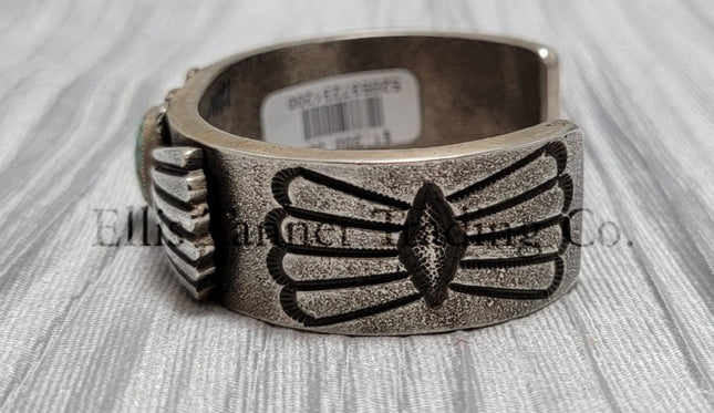 Heavy silver bracelet, with a center Carico Lake Turquoise stone, with an overlay design, on top of a shiny silver sheet side view 