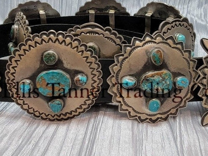A handcrafted Navajo concho belt with detailed sterling silver conchos, each embedded with mixed turquoise stones of varying shades and natural patterns, attached to a black leather strap.
