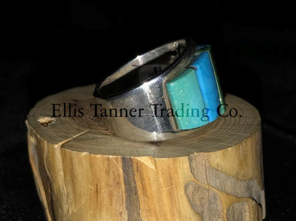 A silver-banded ring with blue and green stone inlays, displayed on a wooden piece, with the brand name 'Inner Trading' visible.