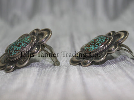 Silver stamped clip on earrings, with a center #8 Turquoise surrounded by a silver rope. side view on top of a silver sheet 