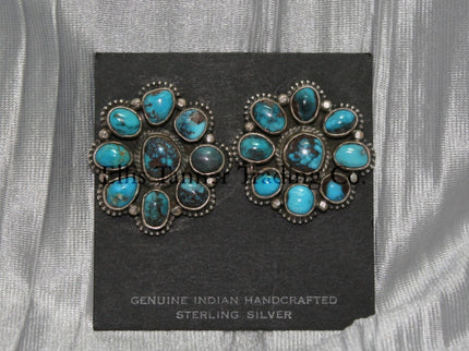 Cluster-style sterling silver clip-on earrings featuring polished turquoise stones with brown matrix patterns, arranged in a floral design with bead accents, displayed on a black card against a silver satin background.
