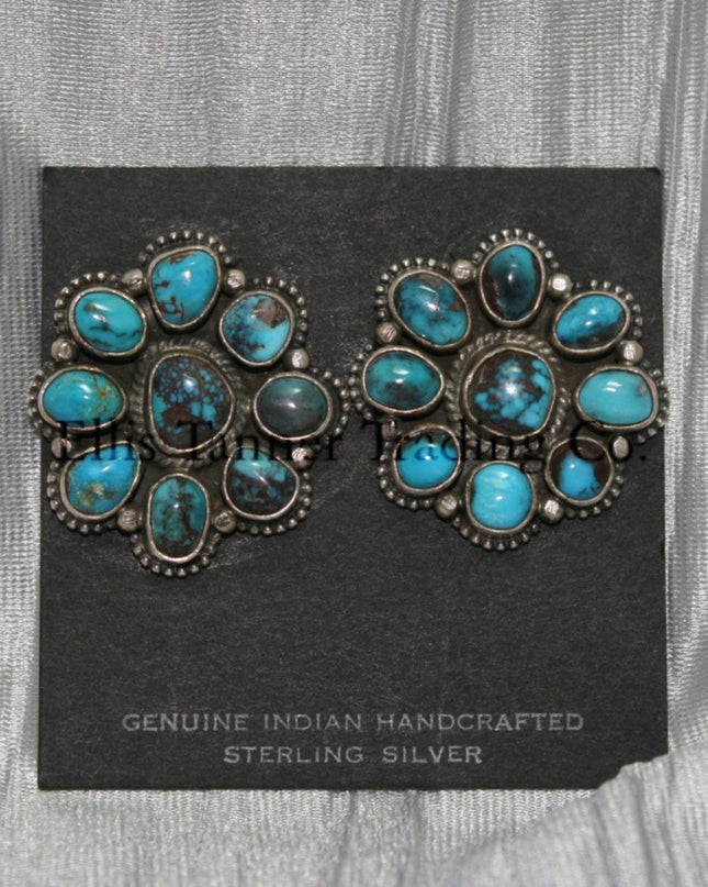 Cluster-style sterling silver clip-on earrings featuring polished turquoise stones with brown matrix patterns, arranged in a floral design with bead accents, displayed on a black card against a silver satin background.