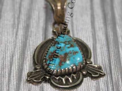Silver Pendant, over lay silver with hand stamped designs. A center Kingman stone surrounded by a silver bezel. placed on top of a shiny cloth 