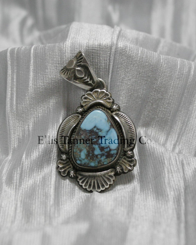 Teardrop-shaped Bisbee turquoise pendant set in sterling silver with intricate engraved details, scalloped accents, and an ornate bail, displayed on a white satin background.