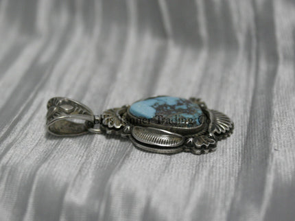 Teardrop-shaped Bisbee turquoise pendant set in sterling silver with intricate engraved details, scalloped accents, and an ornate bail, displayed on a white satin background.