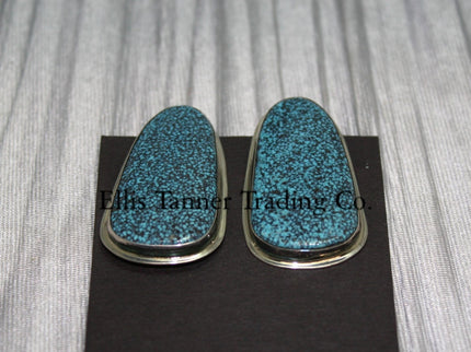 slab-style clip-on earrings featuring polished #8 turquoise stones with a speckled pattern, set in sterling silver bezels, displayed on a black card against a textured silver background. 