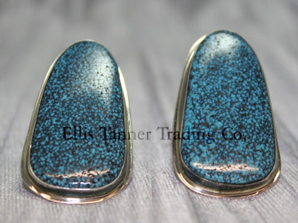 Silver slab-style clip-on earrings featuring polished #8 turquoise stones with a speckled pattern, set in sterling silver bezels, displayed on a black card against a textured silver background.