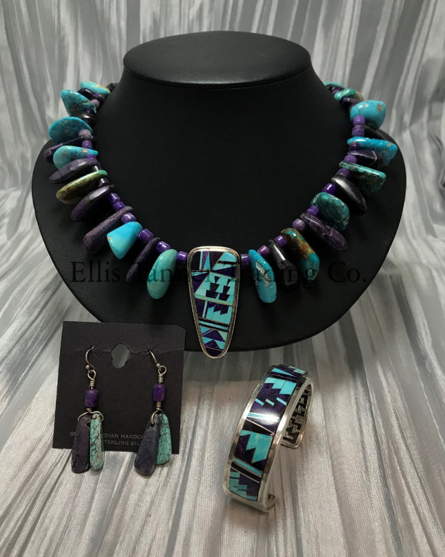A Southwest-style jewelry set featuring a vibrant beaded necklace, earrings, and cuff bracelet. The necklace has Sleeping Beauty turquoise, purple sugilite stones, with a central pendant showcasing intricate geometric inlay work. The matching drop earrings feature Sleeping Beauty turquoise and purple Sugilite beads. The cuff bracelet highlights bold geometric patterns set in sterling silver.